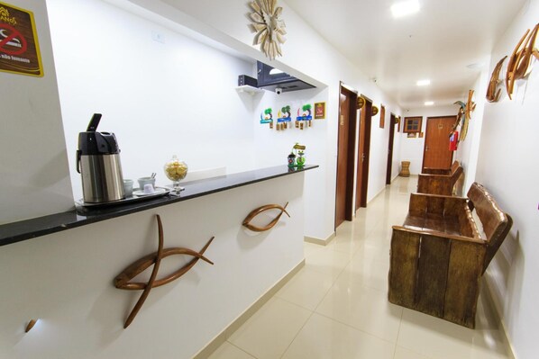 A hotel reception area with a counter, a coffee machine, and a bench. - Cabanos Suites (Maragogi)