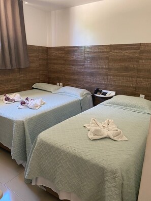 Dos camas individuales con ropa de cama verde claro, un cabecero de madera, una mesita de noche con un teléfono y una toalla sobre una cama.