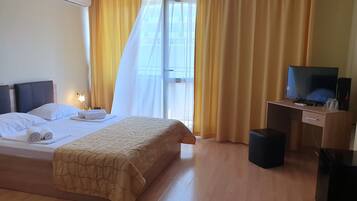 A hotel room with a bed, a desk with a computer, a TV, and a window with curtains.