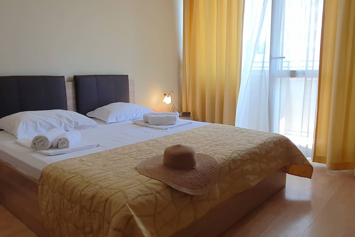 A hotel room with a bed, pillows, a rolled towel, a hat, and a nightstand with a lamp.