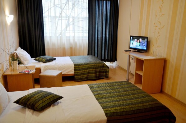 Habitación de hotel con dos camas, un televisor, una mesita con una revista y una ventana con cortinas.