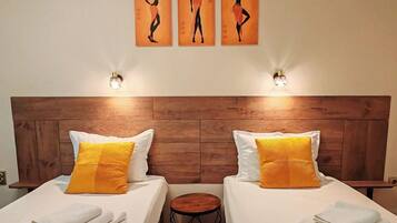 Habitación de hotel con dos camas, cada una con sábanas blancas y almohada amarilla, cabecero de madera y obras de arte colgadas en la pared sobre las camas.