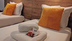 A hotel room with two beds, each with white bedding and a single orange pillow. A folded towel and a brochure are on the bed. - Hotel Sorbona (Varna)