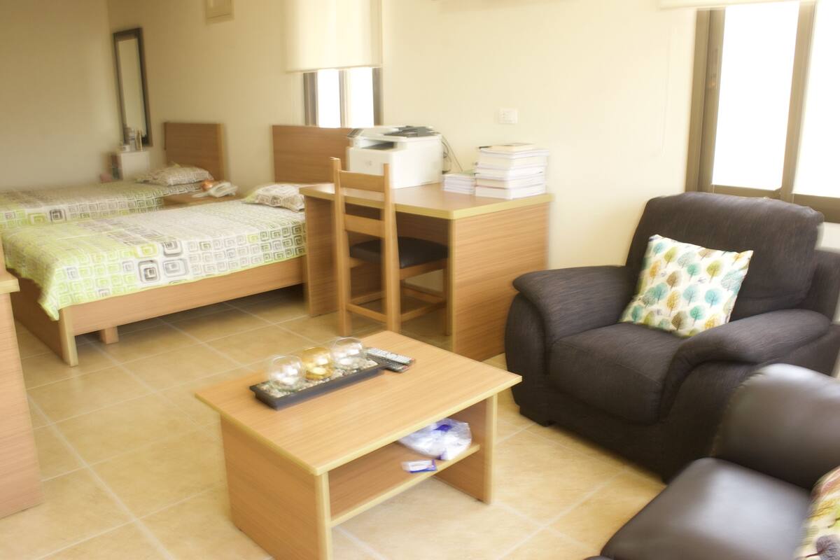 A hotel room with a bed, a desk, a chair, and a small table.
