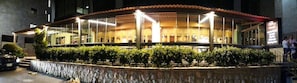 A restaurant with a curved roof, outdoor seating, and a stone wall in front. - Majesty Villa Dorms (Blat)