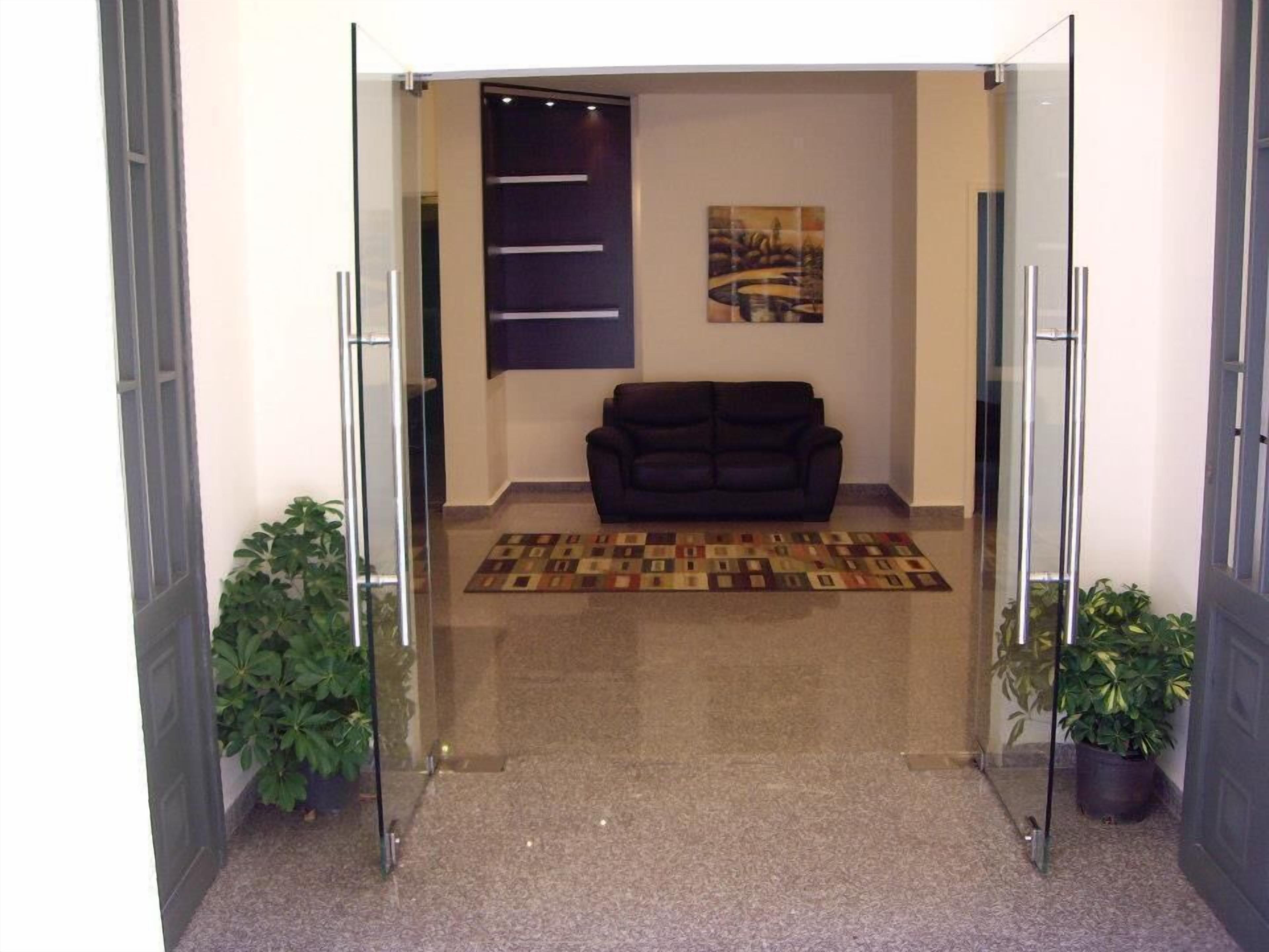 Un hall con un sofá de color oscuro, una alfombra estampada y dos plantas en macetas.
