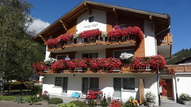Un edificio de dos pisos con un letrero que dice "berg-lyll". Tiene balcones con jardineras y un jardín bien cuidado.