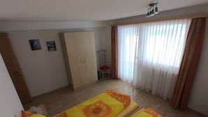 Una habitación con dos camas, un armario, una silla y un ventanal con cortinas.