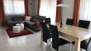 Una sala de estar moderna con un sofá, una mesa de comedor con sillas y una alfombra roja.
