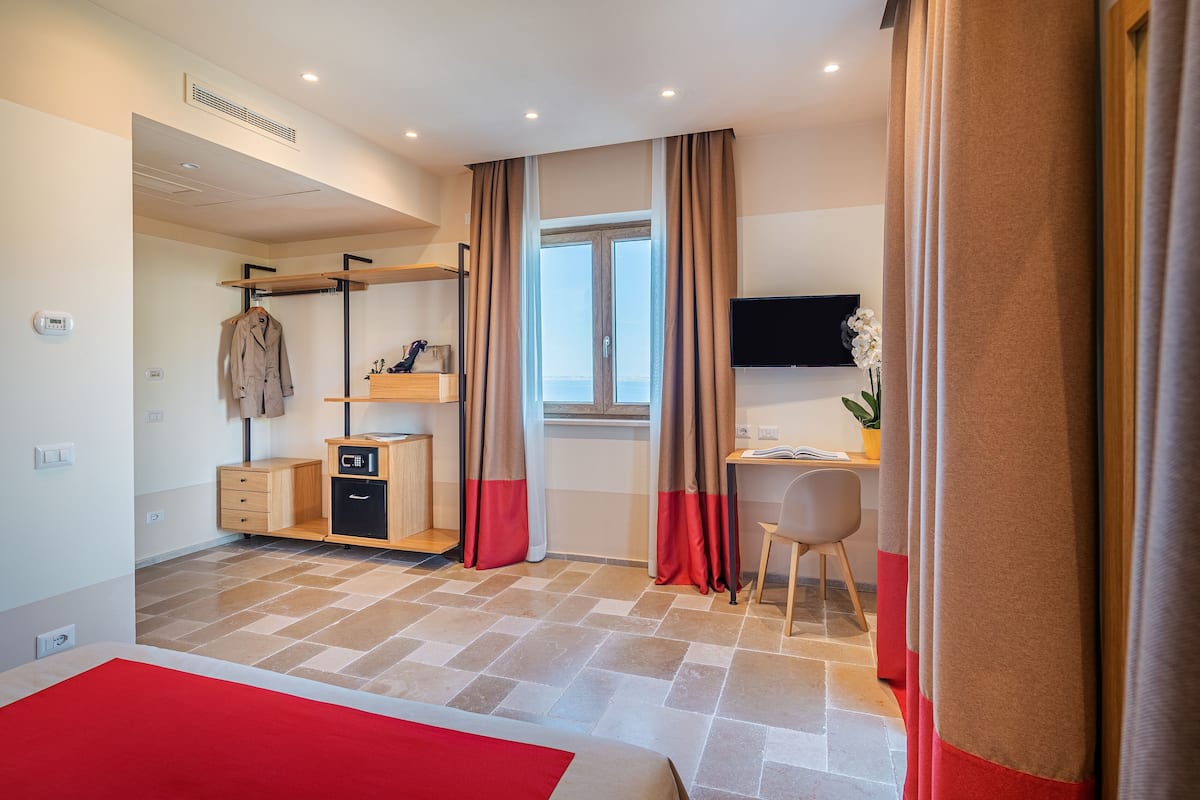 A modern hotel room with a bed, a desk, a chair, a TV, a wardrobe, and a window with curtains.