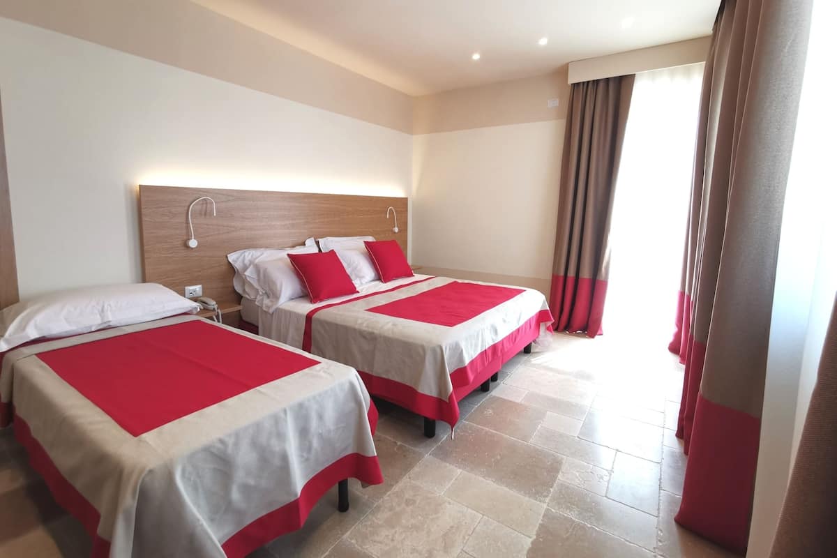 A hotel room with two beds, each with red and white bedding, a wooden headboard, and a nightstand with a phone.