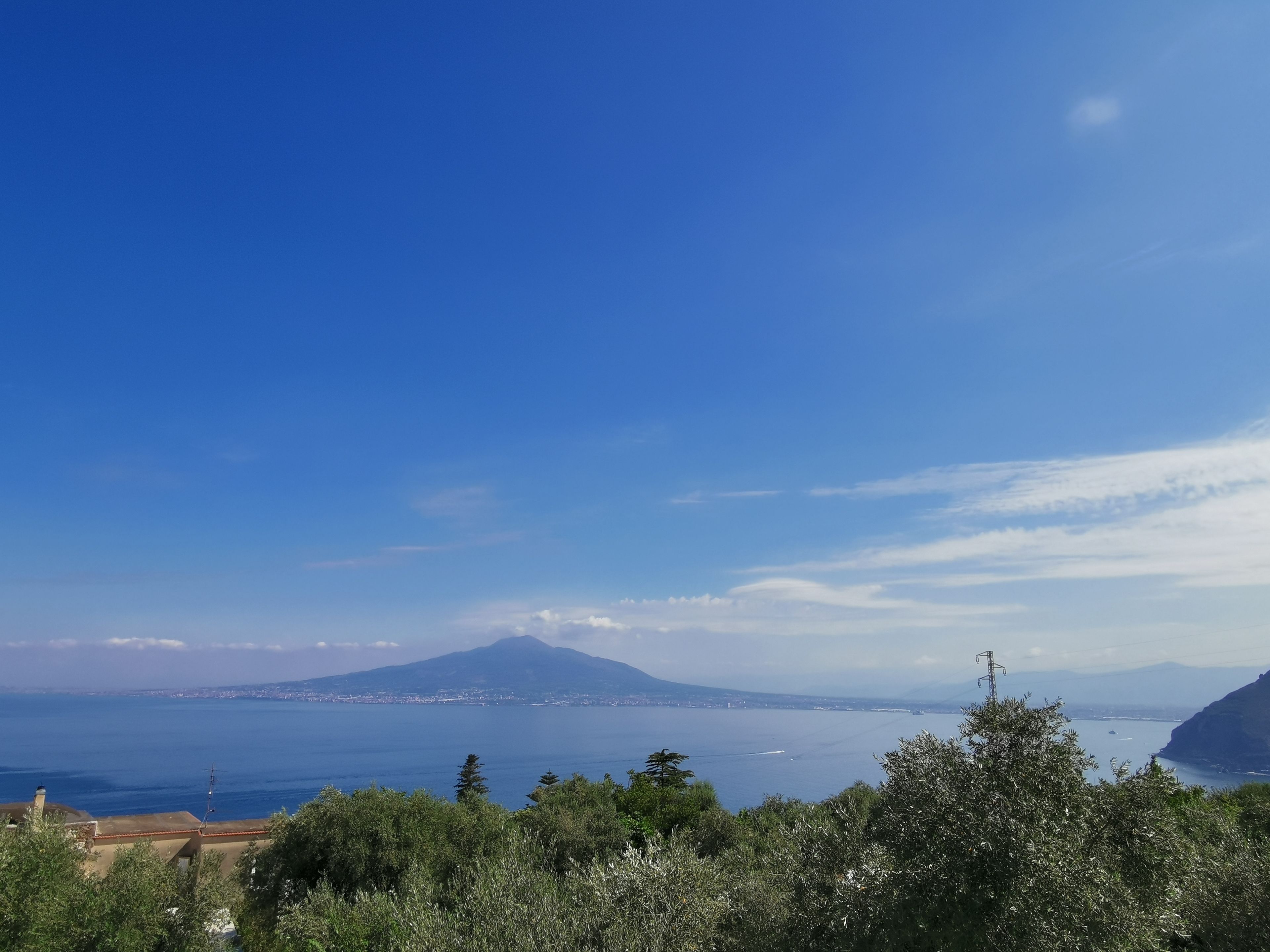 Paesaggio costiero con una montagna all'orizzonte, cielo sereno e vista sul mare.