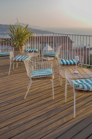 A deck with outdoor seating, including chairs and a table, overlooking a body of water and distant mountains. - Maison Montechiaro (Vico Equense)