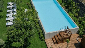 Piscina retangular com um deck de madeira e cadeiras de descanso.