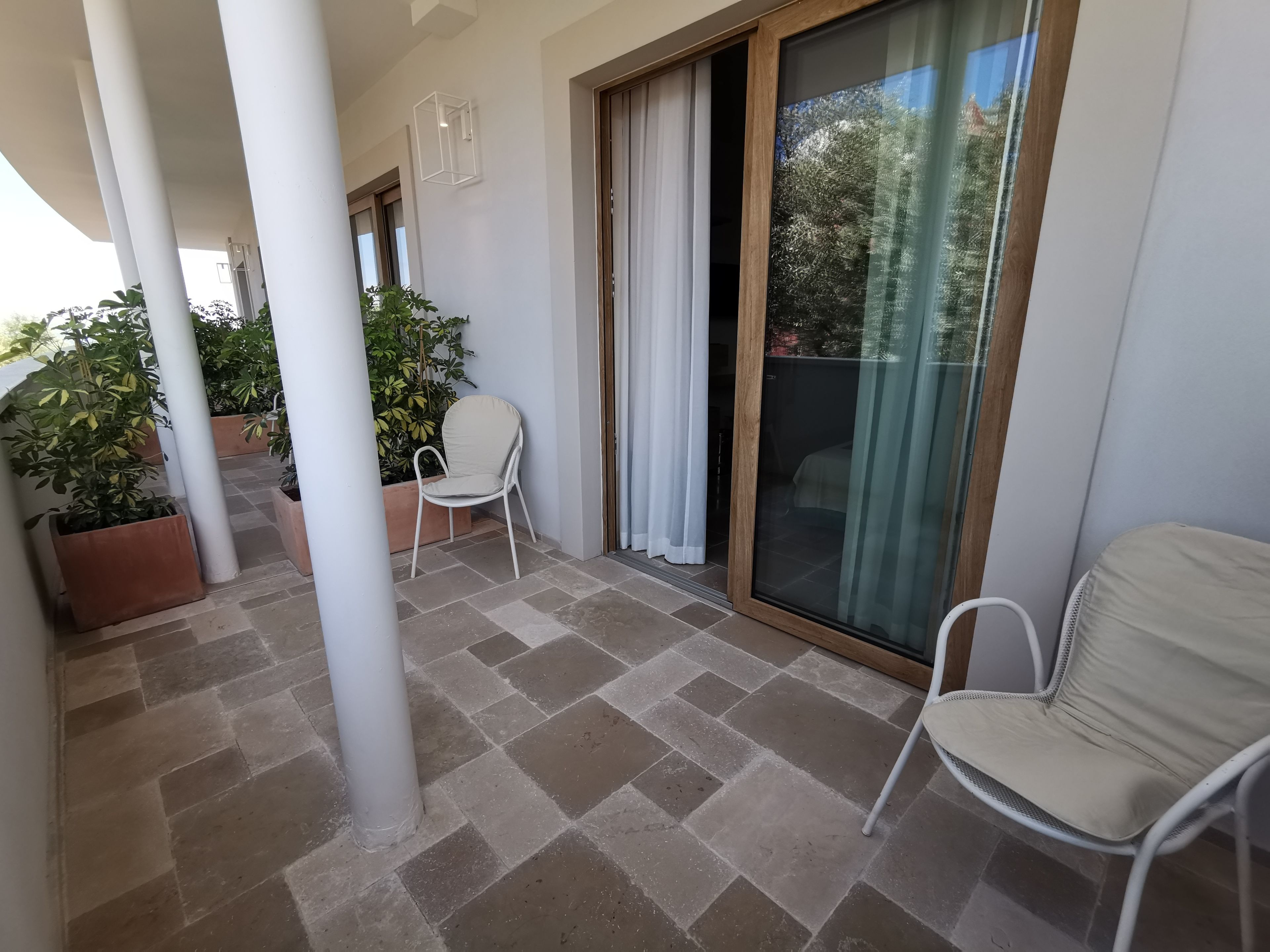 A balcony with tiled flooring, a white chair, and potted plants.