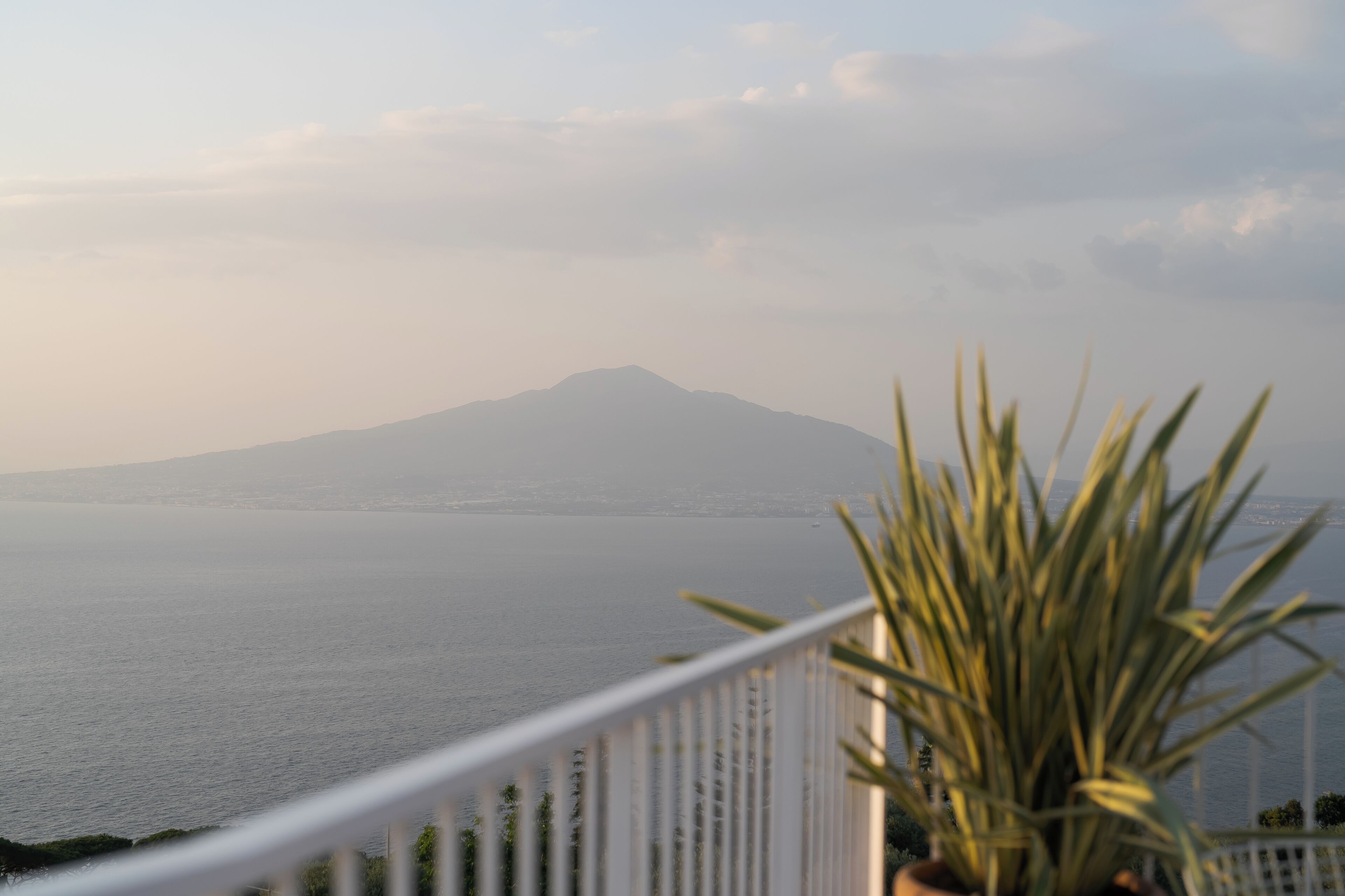 A balcony with a view of a calm sea and a distant mountain.