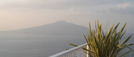 A balcony with a view of a calm sea and a distant mountain.