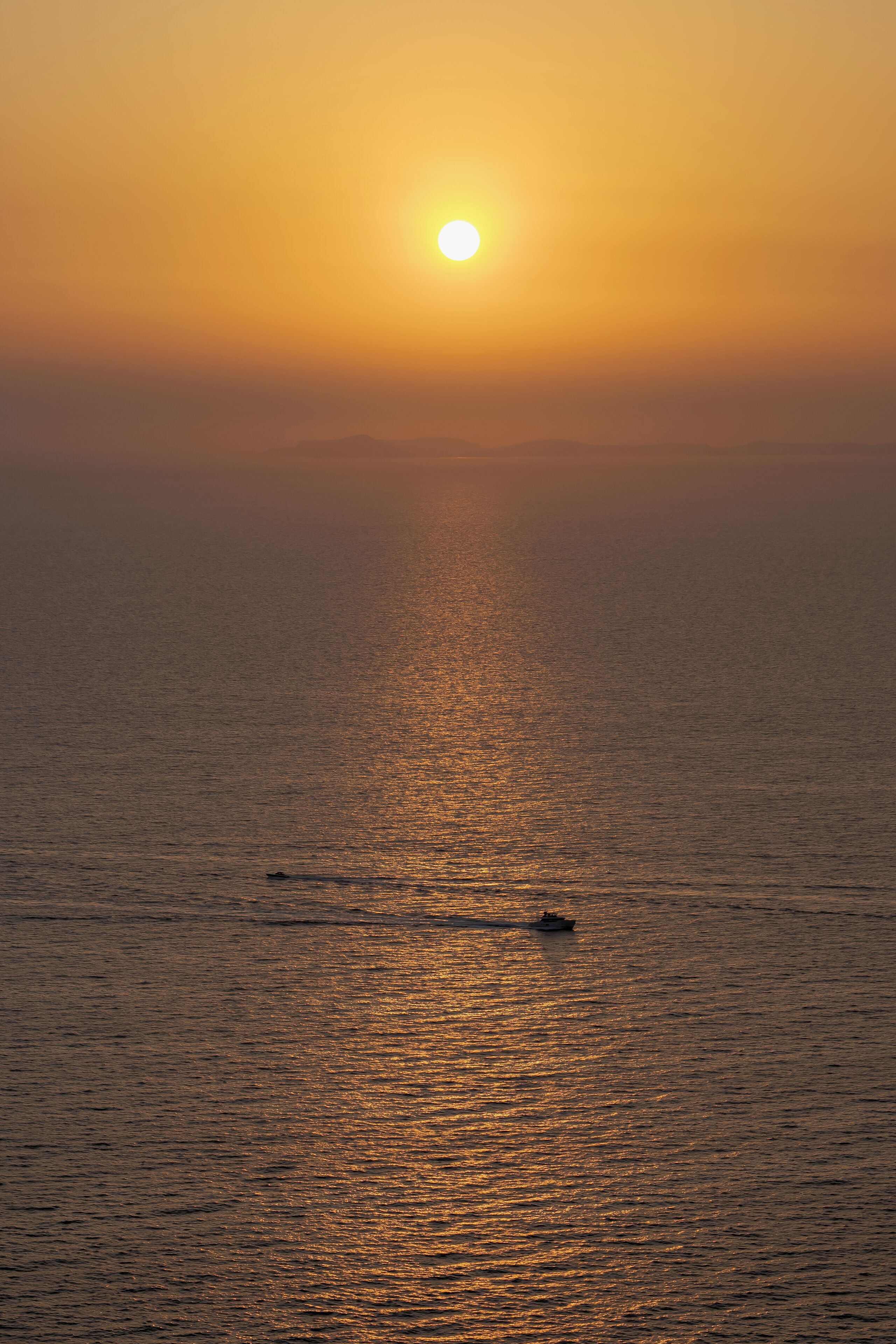 Ein Sonnenuntergang über ruhigem Meer mit einem Schiff in der Ferne.