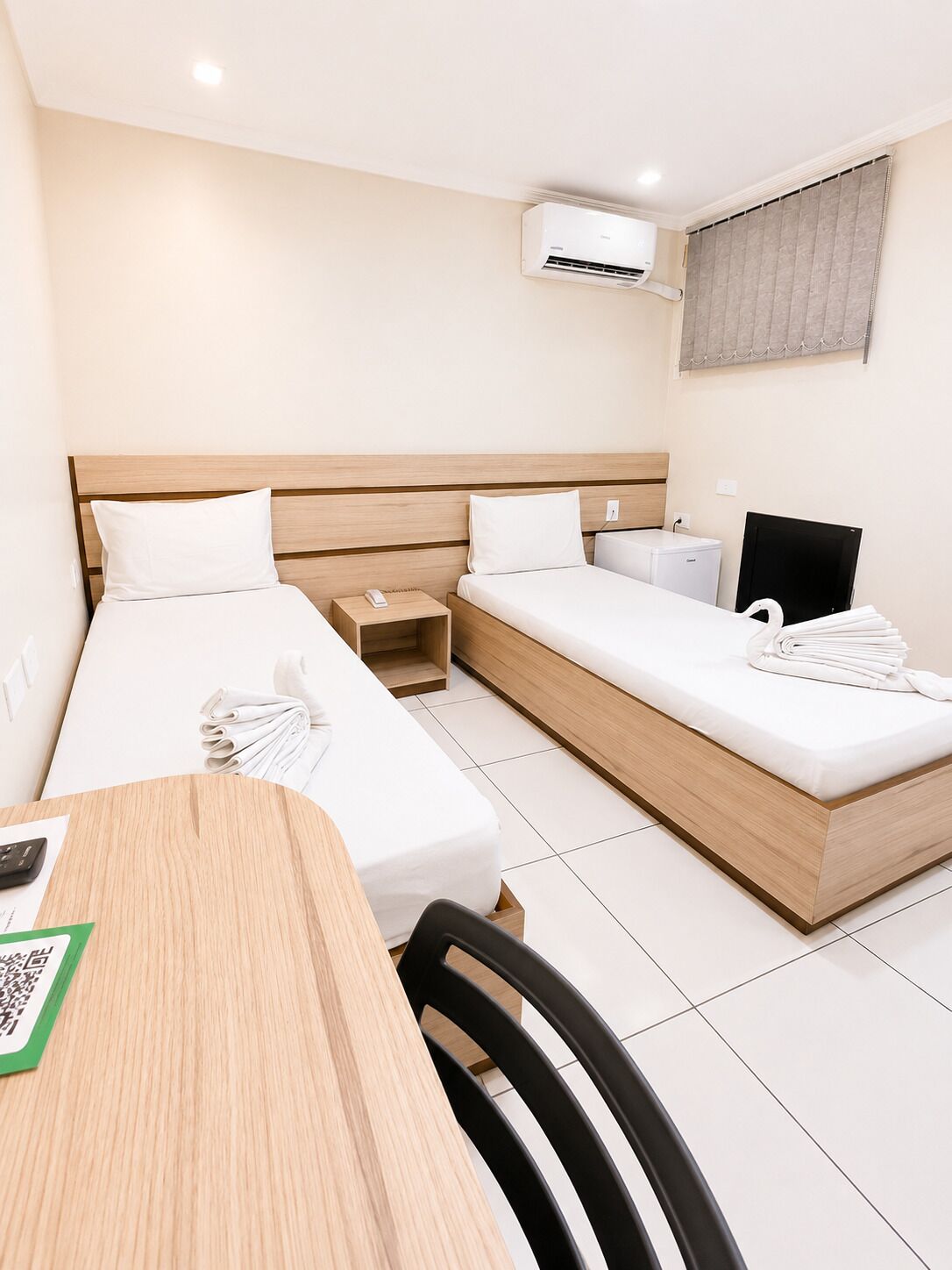 Ein Hotelzimmer mit zwei Betten, einem Schreibtisch, einem Stuhl, einer Klimaanlage und einem Fernseher.
