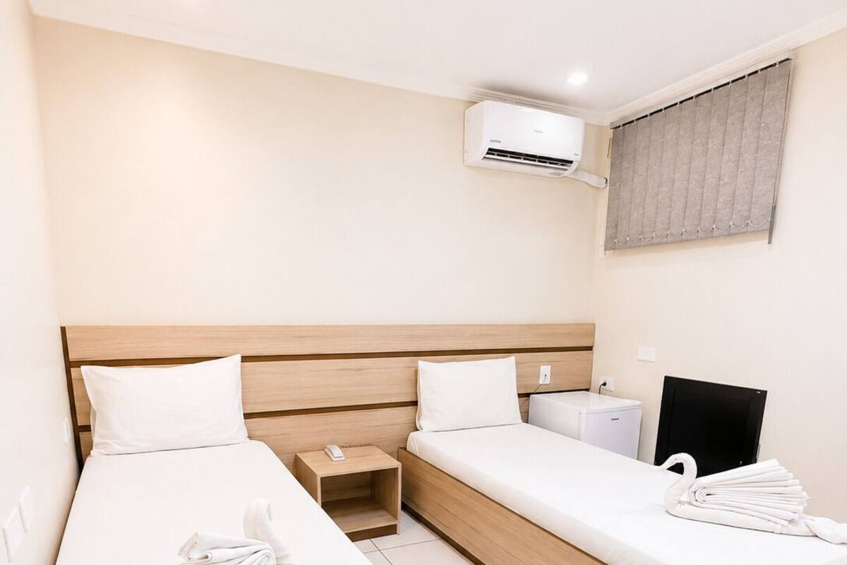 Habitación de hotel con dos camas, un escritorio, una silla, un equipo de aire acondicionado y un televisor.