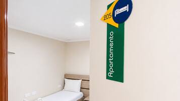 A hotel room with a bed, a small bedside table, a wall-mounted sign indicating room number 205, and a door with a keyhole.