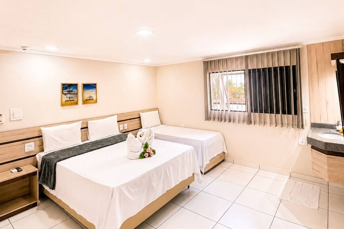 Habitación de hotel con dos camas, baño y ventana con cortinas.