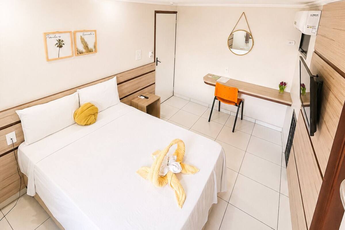 Una habitación de hotel con una cama, un escritorio, una silla, un espejo y un televisor.