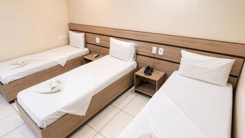 Una habitación de hotel con tres camas individuales, cada una con cabecera de madera, ropa de cama blanca y un control remoto en la mesita de noche.