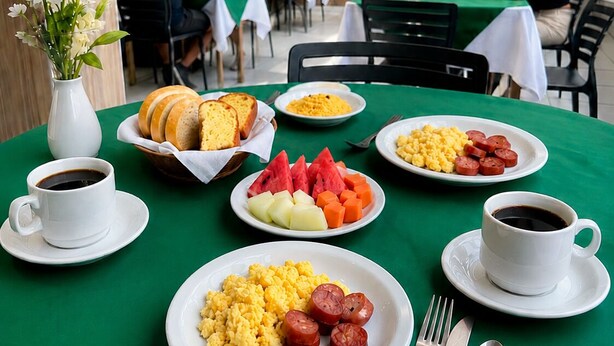A dining area with tables covered in green tablecloths, plates of food, and cups of coffee. - Hotel Nacional (Arapiraca)