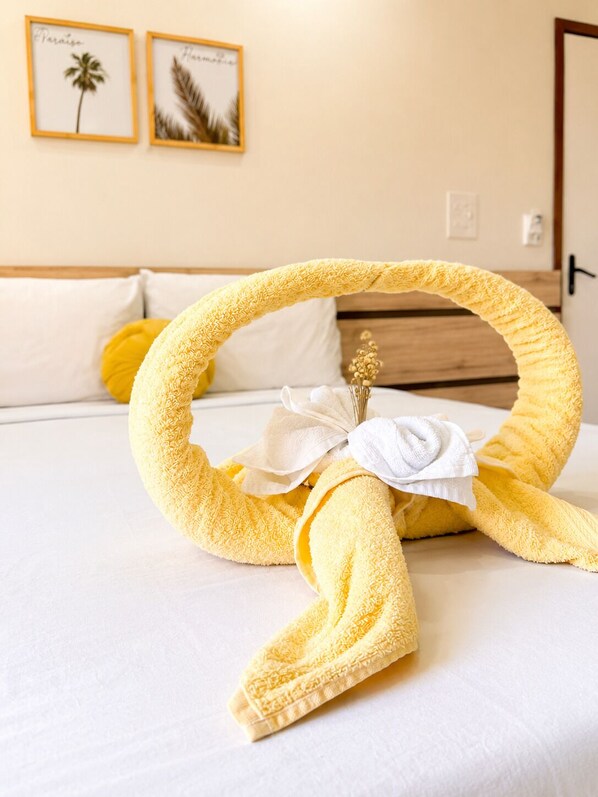 A neatly made bed with a towel arranged in a circular shape, a white pillow, and a yellow pillow.