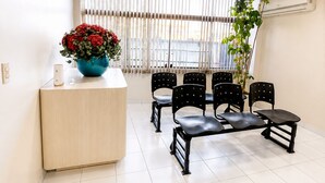 A reception area with a wooden counter, a vase of red flowers, black chairs, and a potted plant. - Hotel Nacional (Arapiraca)