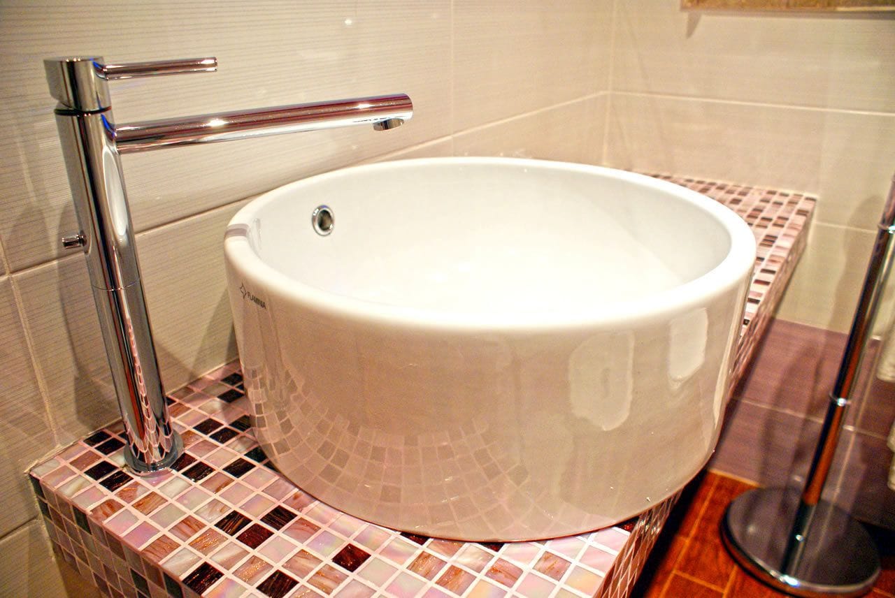 A bathroom with a white sink, chrome faucet, and mosaic tile backsplash.