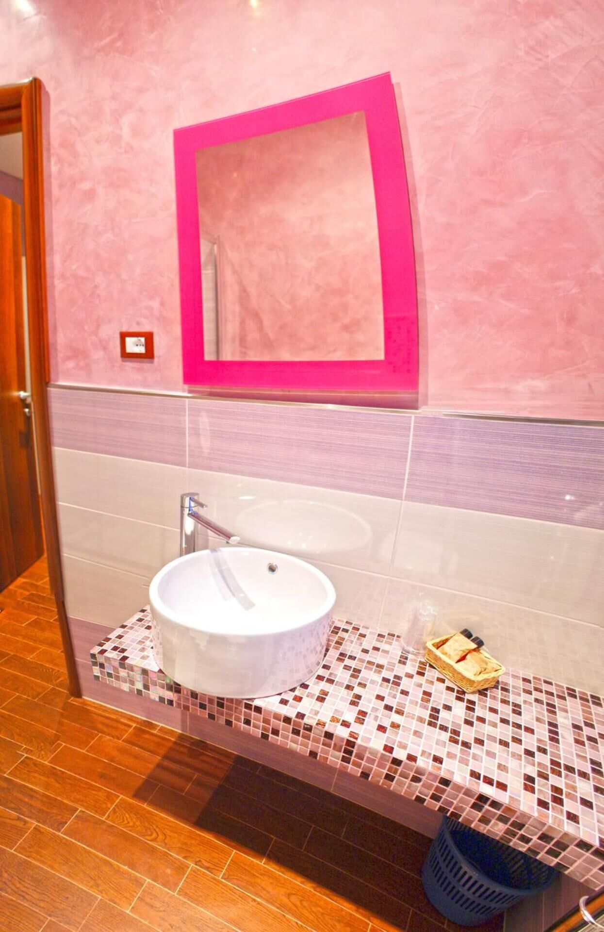 A bathroom with a white sink, a pink-framed mirror, and a tiled floor.