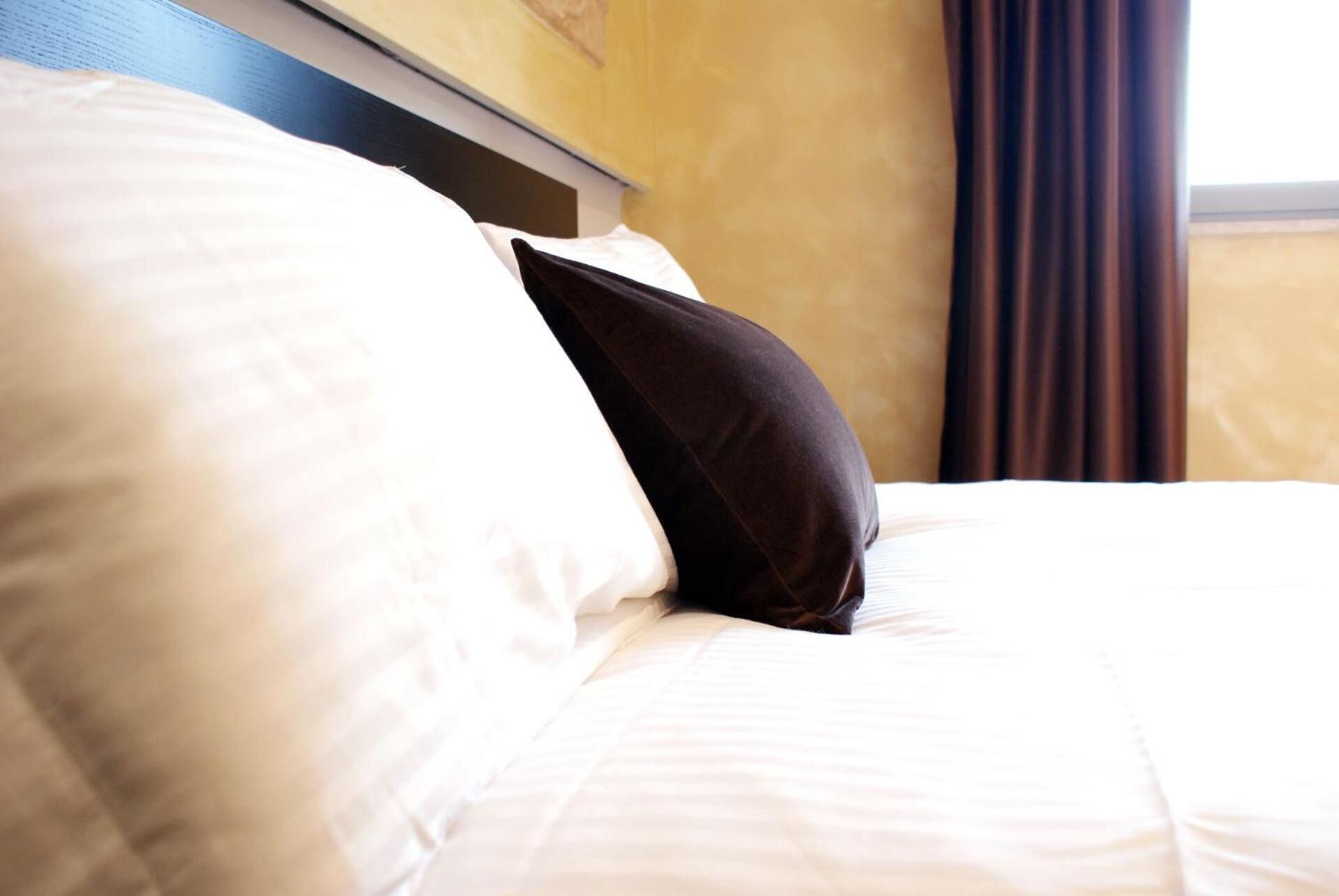 A hotel room with a neatly made bed, white bedding, and a dark brown headboard.