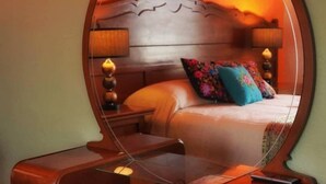 A bedroom with a large round mirror, a wooden headboard, a bed with colorful pillows, and a bedside table with a lamp. - Casa Alfareros (Tlaquepaque)
