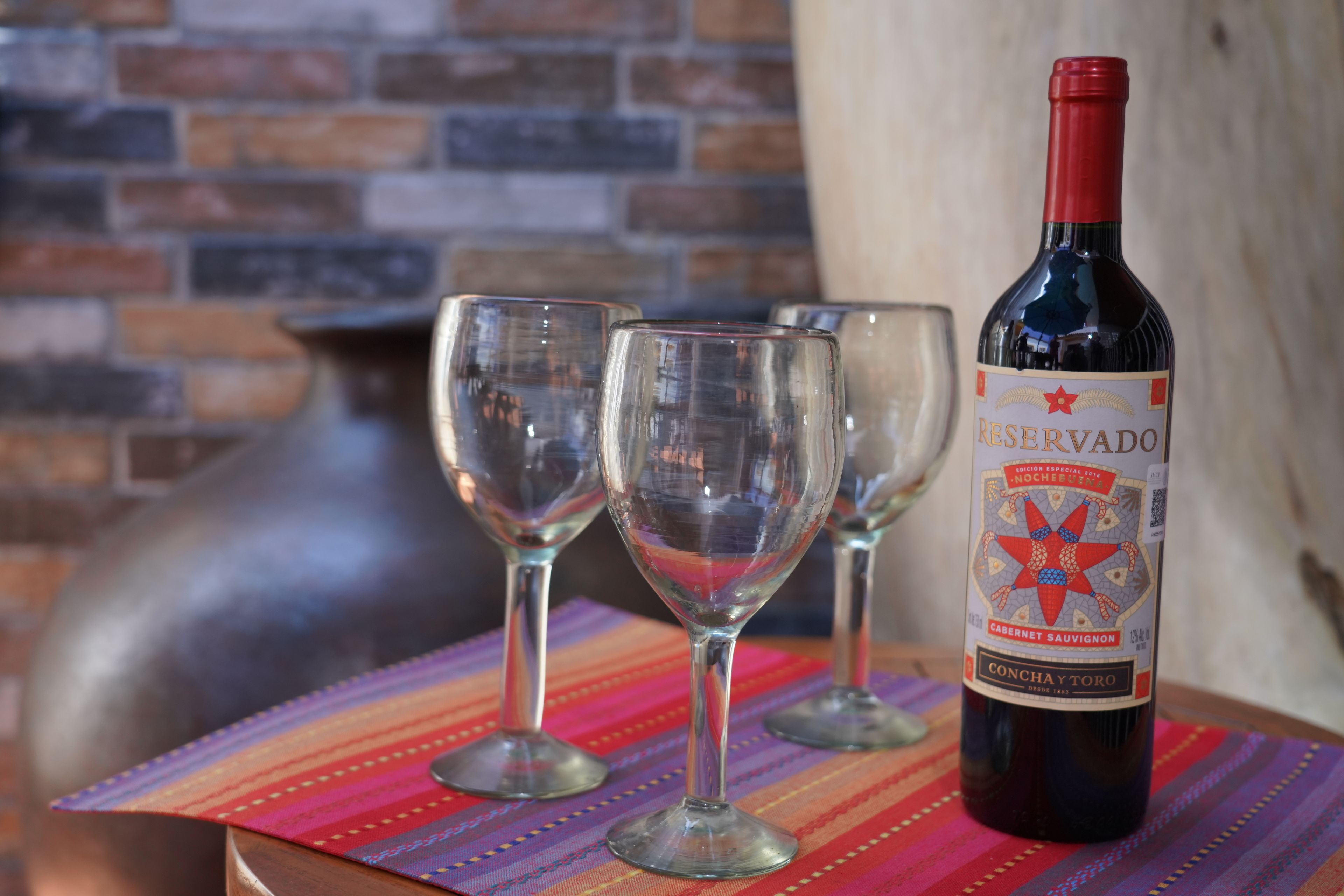 Una botella de vino Conchay Toro sobre una mesa con tres copas de vino vacías.