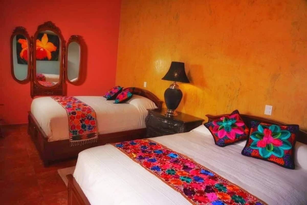 A hotel room with two beds, a mirror, a lamp, and colorful pillows.
