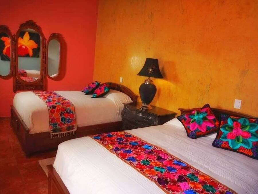 A hotel room with two beds, a mirror, a lamp, and colorful pillows.