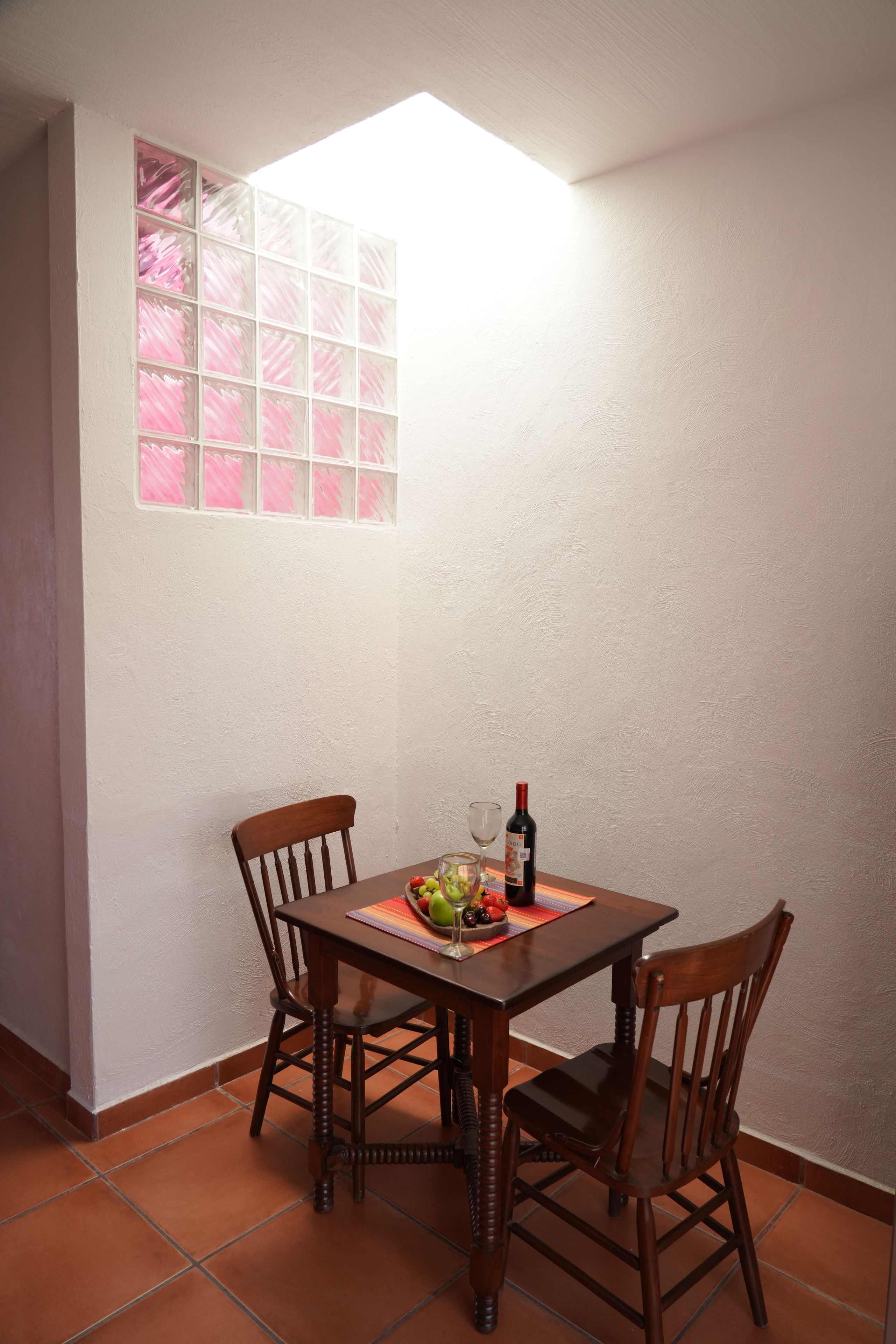 Un coin repas avec une table dressée pour deux personnes, une bouteille de vin et un panier de fruits.