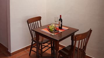 Un coin repas avec une table dressée pour deux personnes, une bouteille de vin et un panier de fruits.