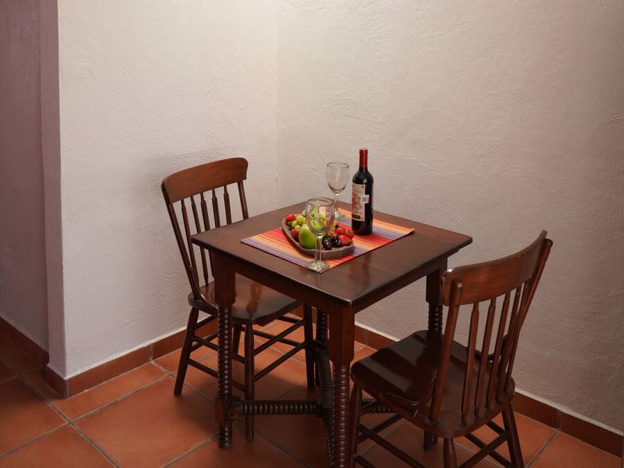 Un coin repas avec une table dressée pour deux personnes, une bouteille de vin et un panier de fruits.