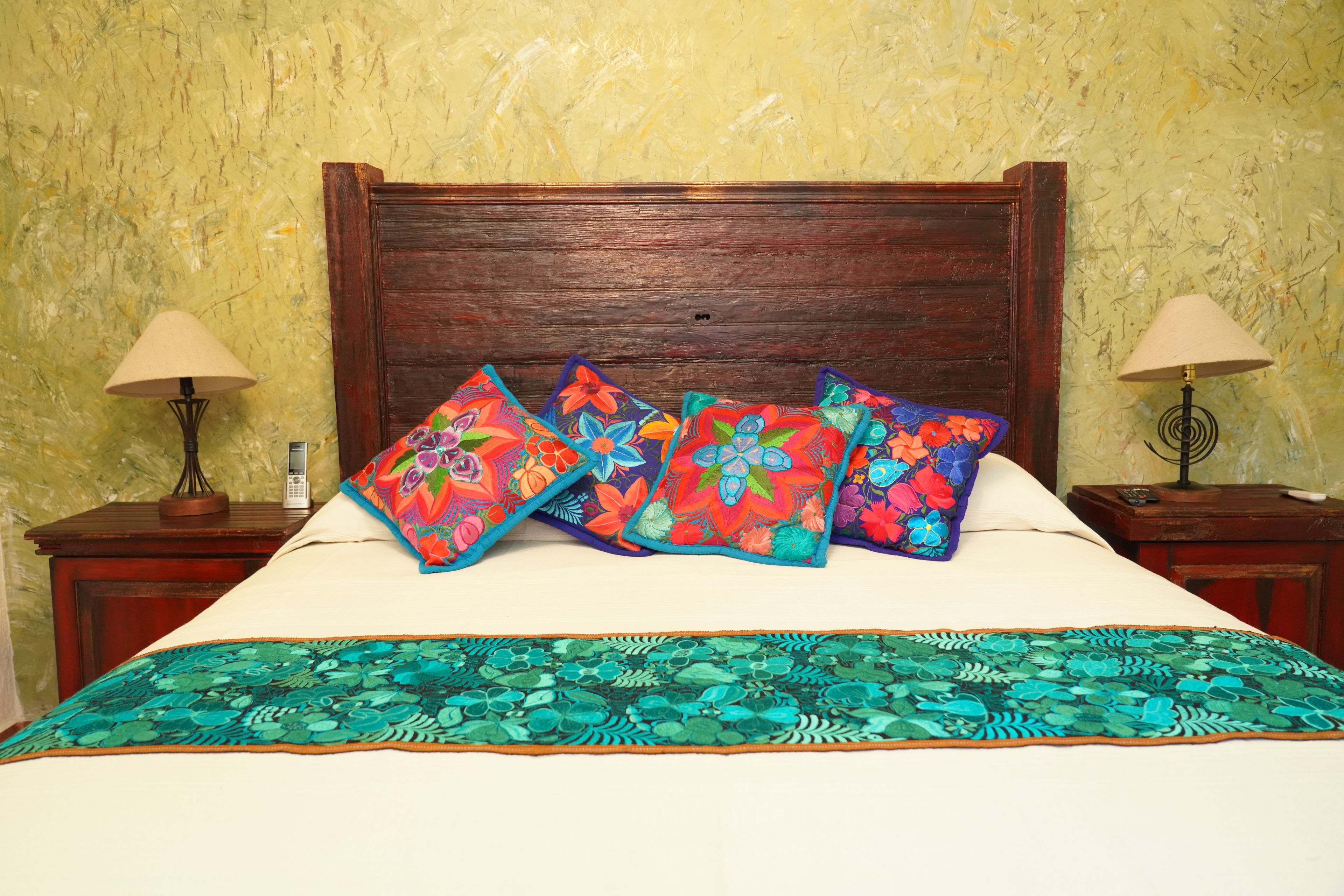 A bed with a wooden headboard, multiple colorful pillows, and a patterned bedspread.