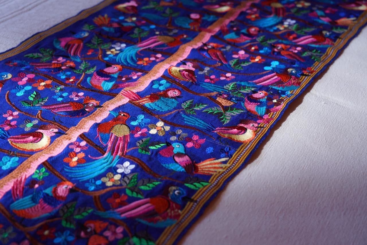 A detailed embroidered fabric with colorful birds and floral patterns.