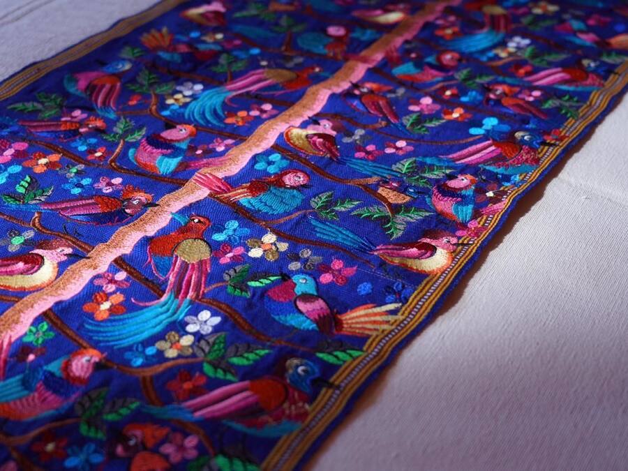 A detailed embroidered fabric with colorful birds and floral patterns.
