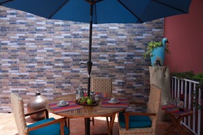 An outdoor patio with a brick wall, a round wooden table, wicker chairs, and a blue umbrella. - Casa Alfareros (Tlaquepaque)