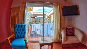 A room with a blue chair, a white chair, a small table, and a TV on the wall. - Casa Alfareros (Tlaquepaque)