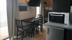 A compact kitchen with a microwave, a small refrigerator, and a dining area with wooden chairs and a table. - Black Beach Small Cottage (Sveitarfélagid Ölfus)
