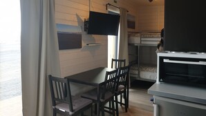 A compact room with a bunk bed, a dining table with chairs, a kitchenette with a stove, and a television mounted on the wall. - Black Beach Small Cottage (Sveitarfélagid Ölfus)