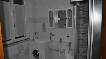 Un bagno compatto con lavatrice, lavandino e specchio.