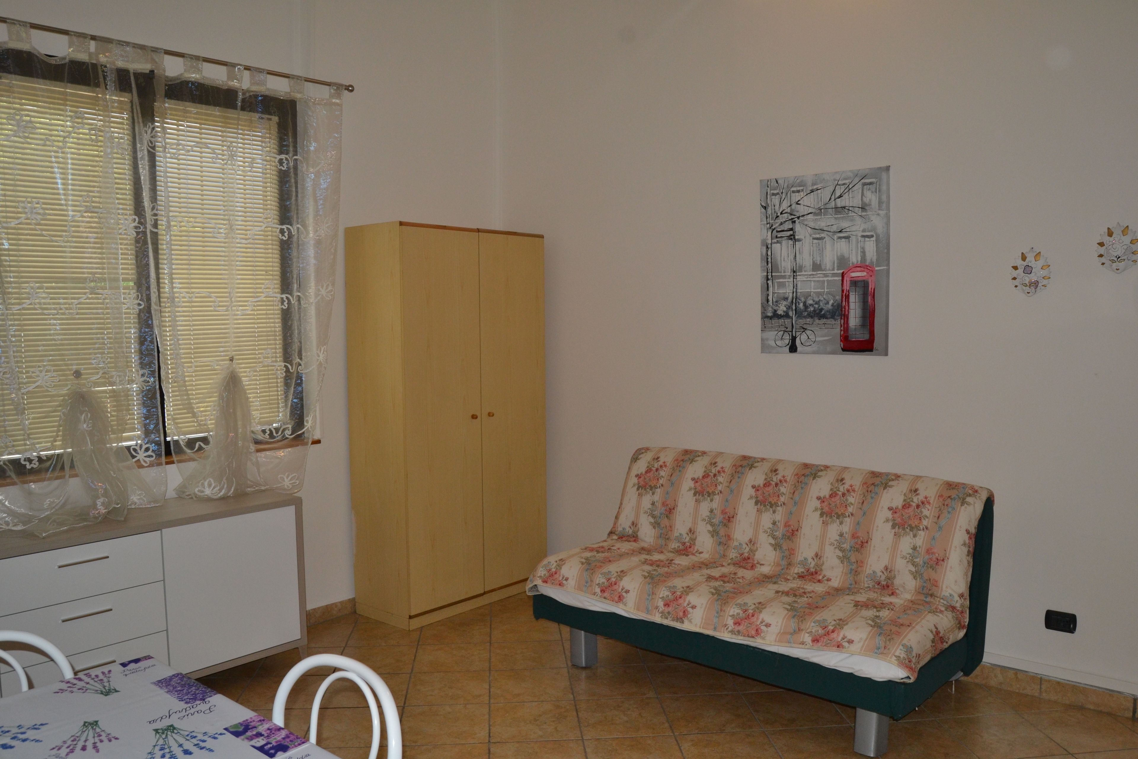 Une pièce comprenant une armoire en bois, un canapé à motifs floraux, une table à manger avec des chaises et une fenêtre avec des stores.